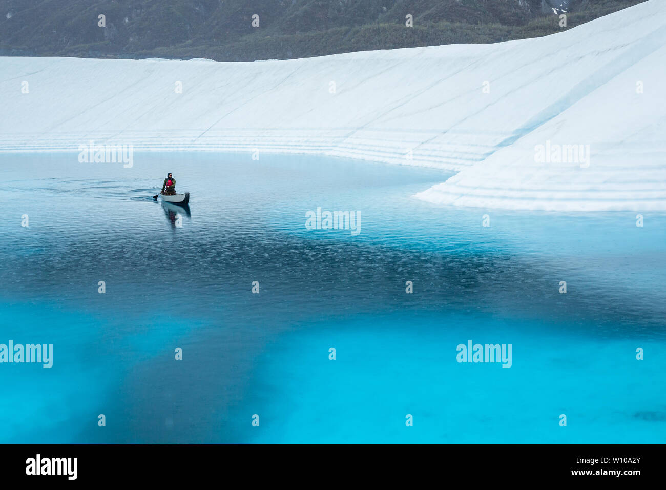 Pagaiando attraverso un lago supraglacial sul ghiacciaio Matanuska sotto la pioggia. Ice Climber corssing un profondo lago blu getting piovuto a. Foto Stock