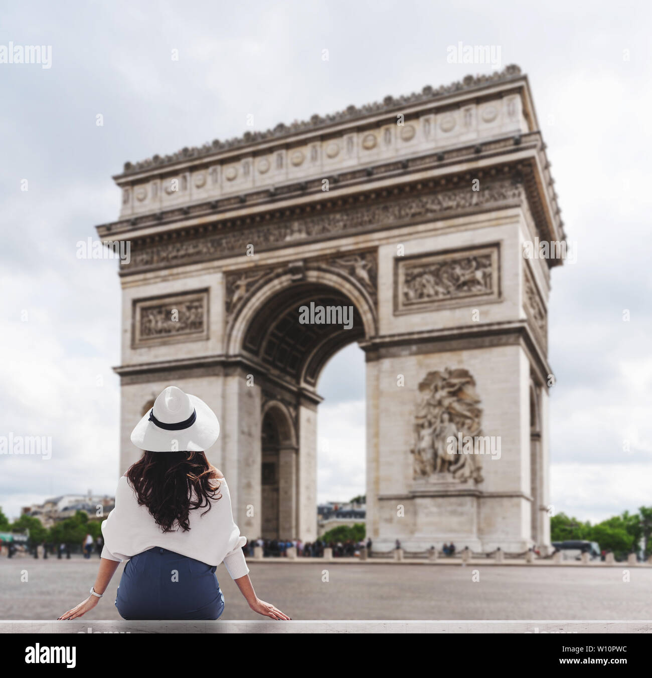 Giovane donna di viaggiatori nel cappello bianco guardando a Arc de Triomphe, famoso punto di riferimento e meta di viaggio a Parigi in Francia in estate Foto Stock
