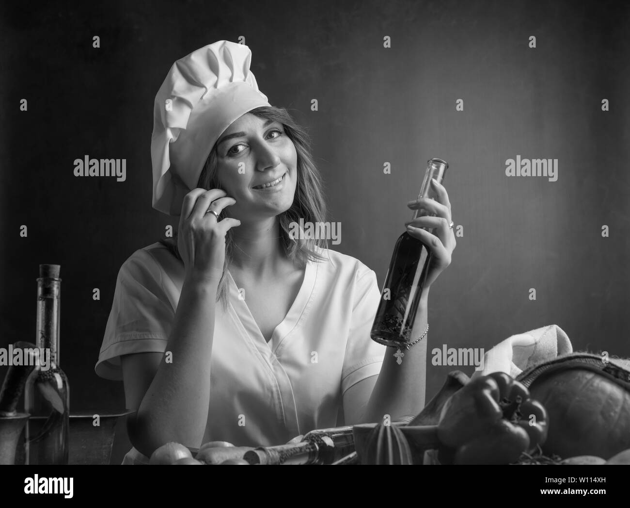 Giovane donna in uno chef uniforme con piccole bottiglie di olio d'oliva. Fragrante olio di oliva con varie spezie e erbe aromatiche. In bianco e nero. Foto Stock