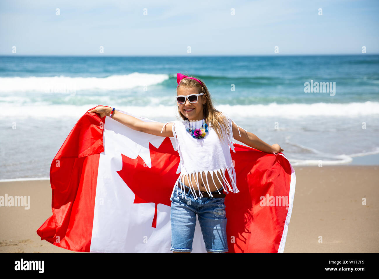 Felice ragazza canadese porta svolazzanti bianco rosso bandiera del Canada contro il cielo blu e Sfondo oceano. Bandiera canadese è un simbolo di libertà e la libertà Foto Stock