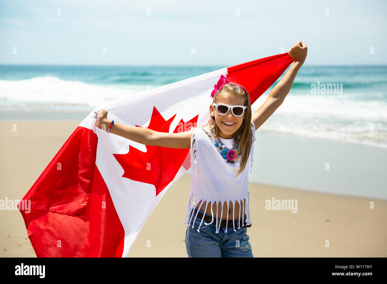Felice ragazza canadese porta svolazzanti bianco rosso bandiera del Canada contro il cielo blu e Sfondo oceano. Bandiera canadese è un simbolo di libertà e la libertà Foto Stock