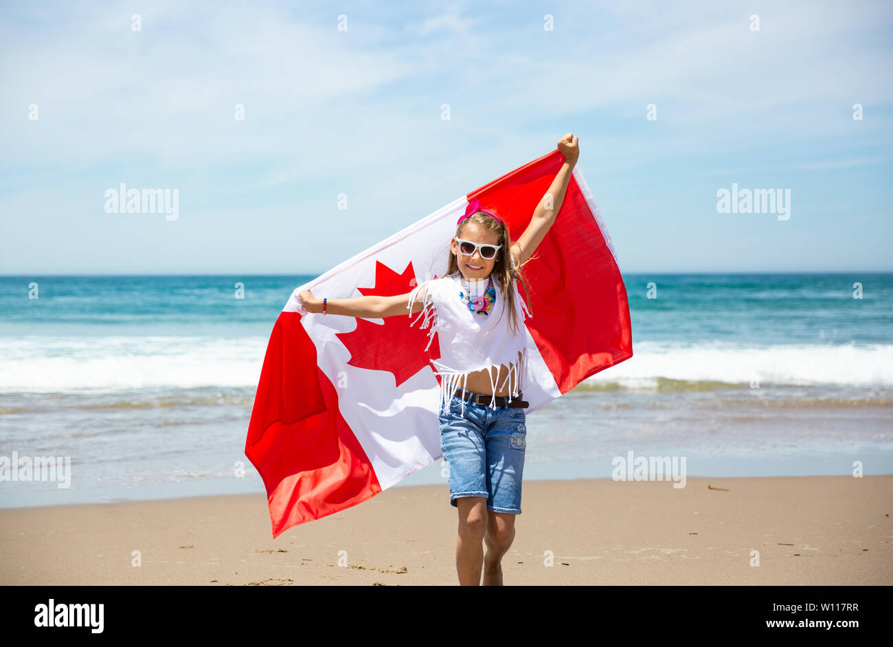 Felice ragazza canadese porta svolazzanti bianco rosso bandiera del Canada contro il cielo blu e Sfondo oceano. Bandiera canadese è un simbolo di libertà e la libertà Foto Stock