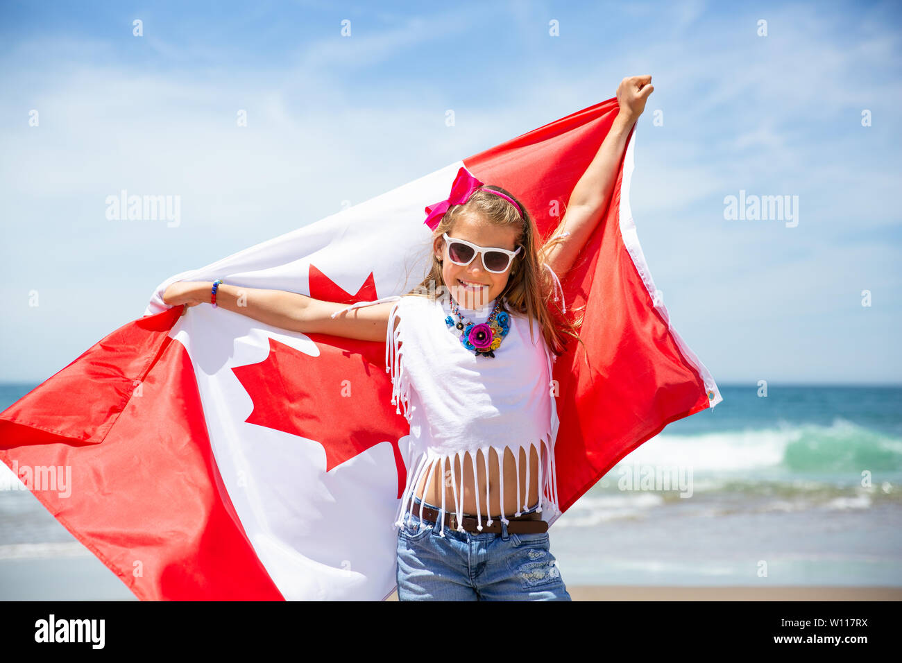 Felice ragazza canadese porta svolazzanti bianco rosso bandiera del Canada contro il cielo blu e Sfondo oceano. Bandiera canadese è un simbolo di libertà e la libertà Foto Stock