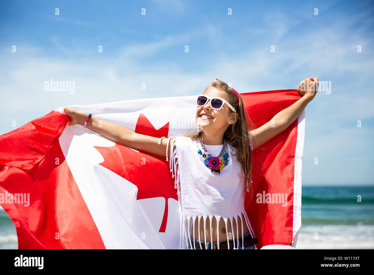 Felice ragazza canadese porta svolazzanti bianco rosso bandiera del Canada contro il cielo blu e Sfondo oceano. Bandiera canadese è un simbolo di libertà e la libertà Foto Stock