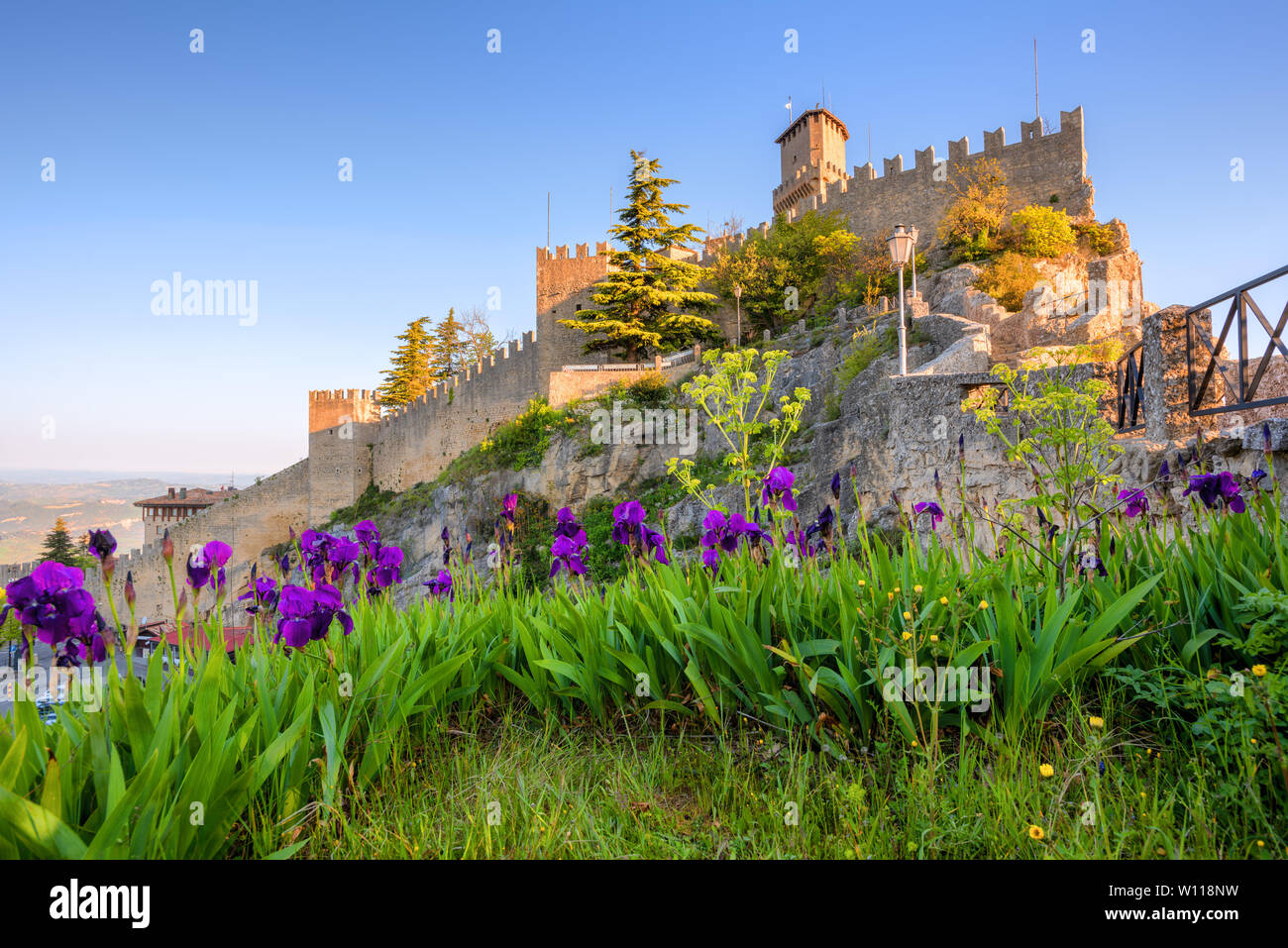 Guaita, la prima delle tre torri di San Marino, sulla cima del monte Titano rock, vista dal giardino con rigogliosi iris fiori, Repubblica di San Foto Stock