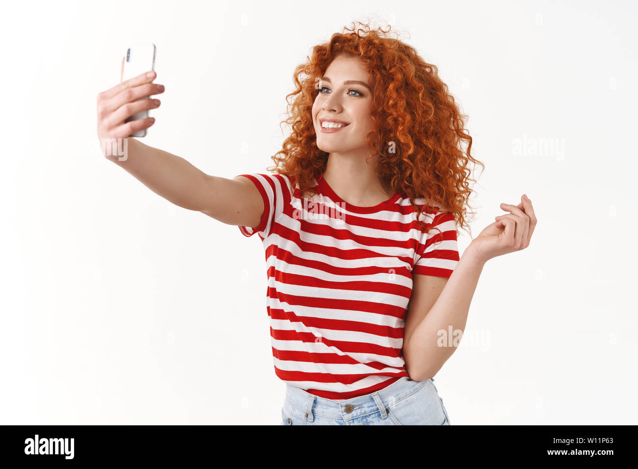 Elegante Attraente redhead, curly-haired girl sciopero alla moda pongono tenendo selfie attesa che mostra lo smartphone social media seguaci nuovo vestito estivo sm Foto Stock