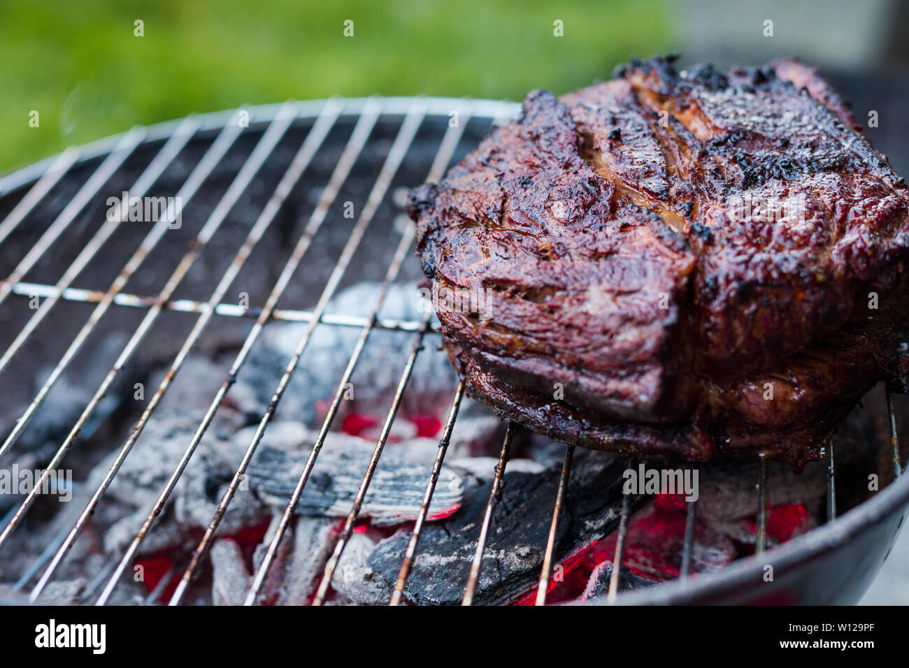 Una grande punta di petto di manzo ed essendo barbequed su un piccolo carbone grill hibachi con carboni ardenti sotto. Foto Stock