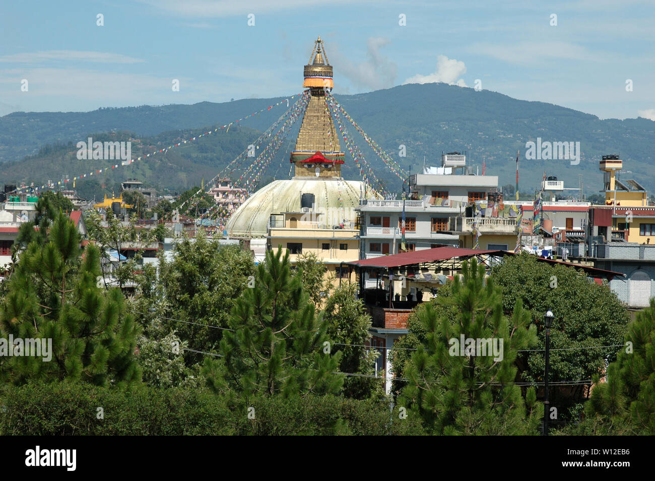 Bodnath stupa contro lo sfondo di piante verdi, cielo blu e nuvole. Il Nepal, Katmandu Foto Stock