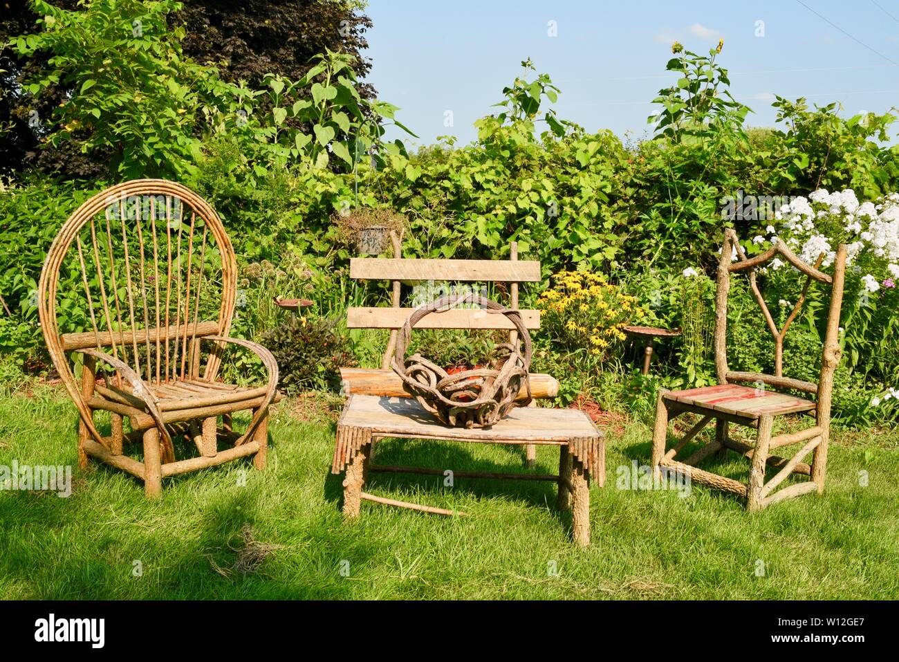 Rustico in legno e lavorati a mano di mobili da esterno tavolo e sedie adagiato in lussureggianti giardini posti a sedere esterni a Squash Blossom Farm, Oronoco, Minnesota, Stati Uniti d'America. Foto Stock