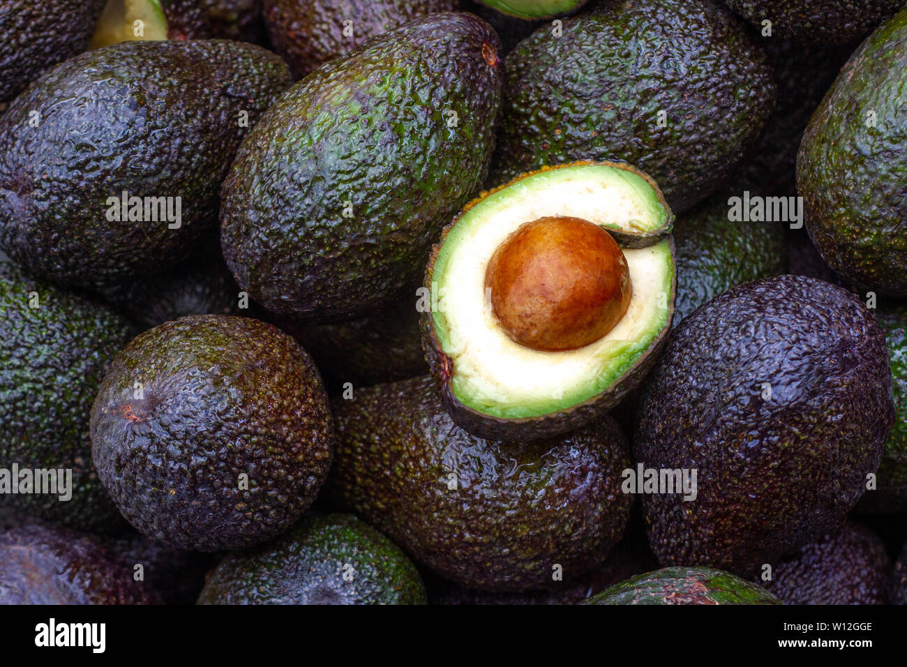 Mezz'avocado con seme visibile giacente sulla sommità di una pila di altri mature Avocadi freschi Foto Stock