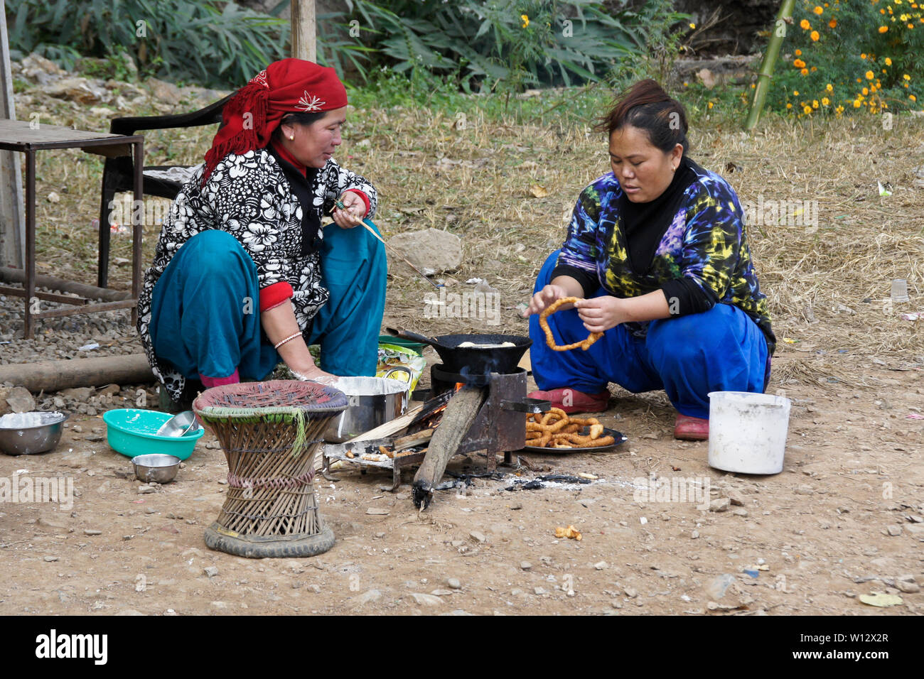 Le donne in abito tradizionale rendendo sel (impasto fritto) presso un ristorante su strada nelle zone rurali del Nepal Foto Stock