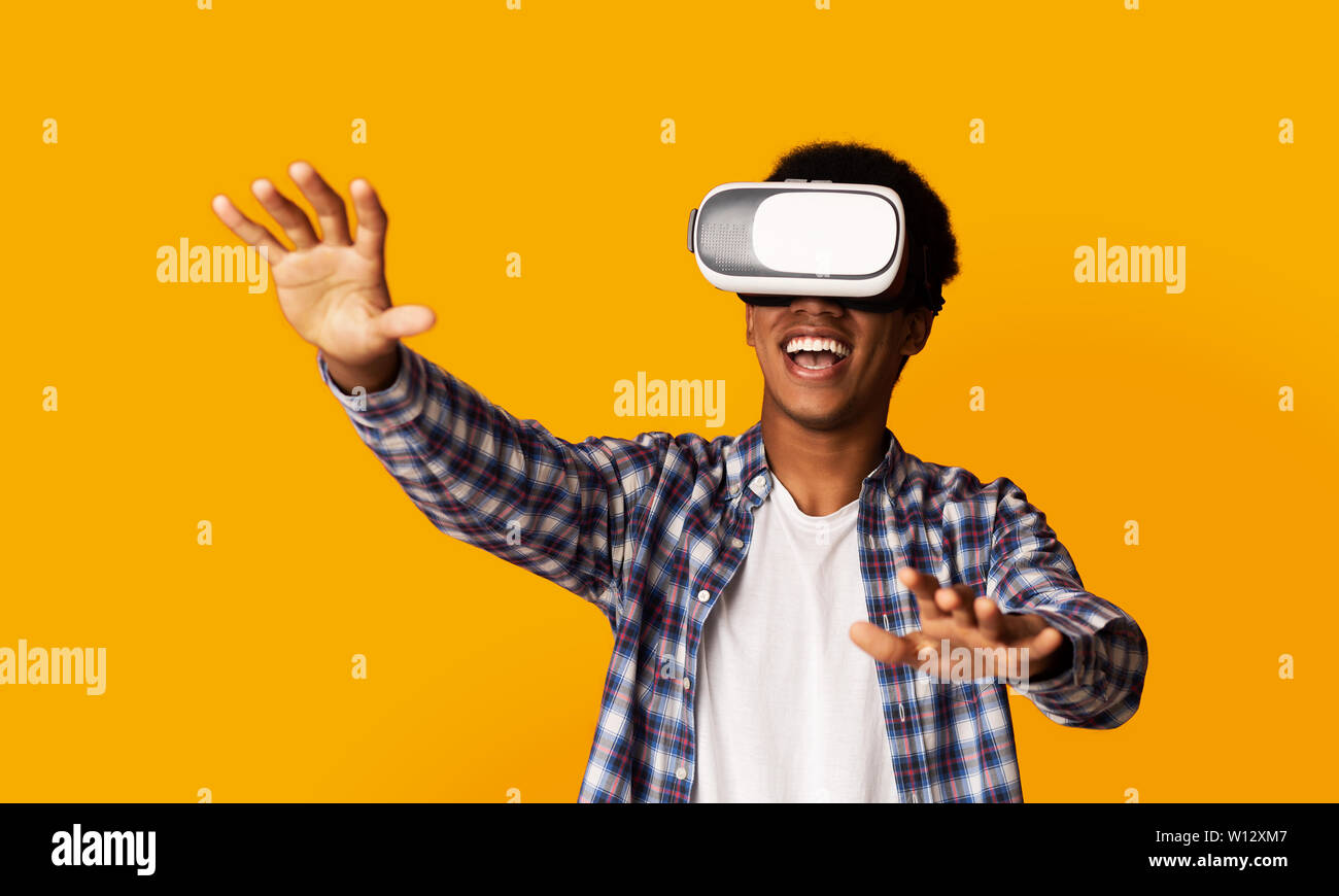 Afro-americano di Guy utilizzando cuffie VR, sfondo giallo Foto Stock