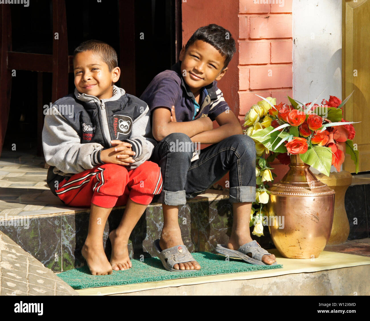 Due giovani ragazzi sedersi sul passo del cafe in Newari storico trading post città di Bandipur, Tanahan District, Nepal Foto Stock