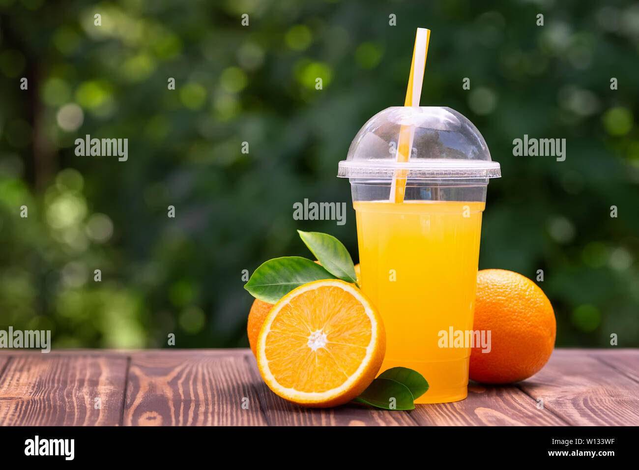 Il succo d'arancia fresco in una tazza di plastica sul tavolo in legno all'esterno. Togliere il vetro con estate bevanda rinfrescante Foto Stock
