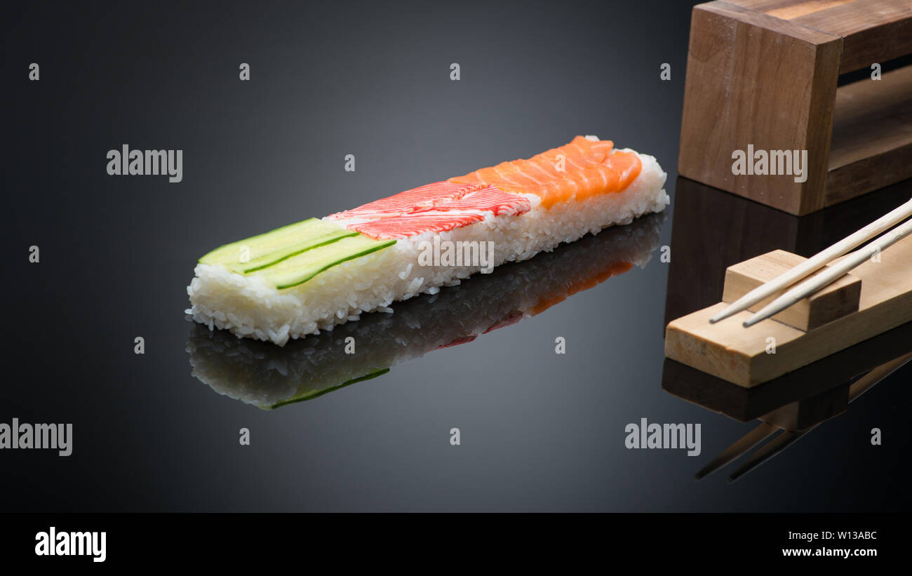 Sushi su sfondo nero con bacchette in legno per premere il modulo per rendere il sushi Foto Stock