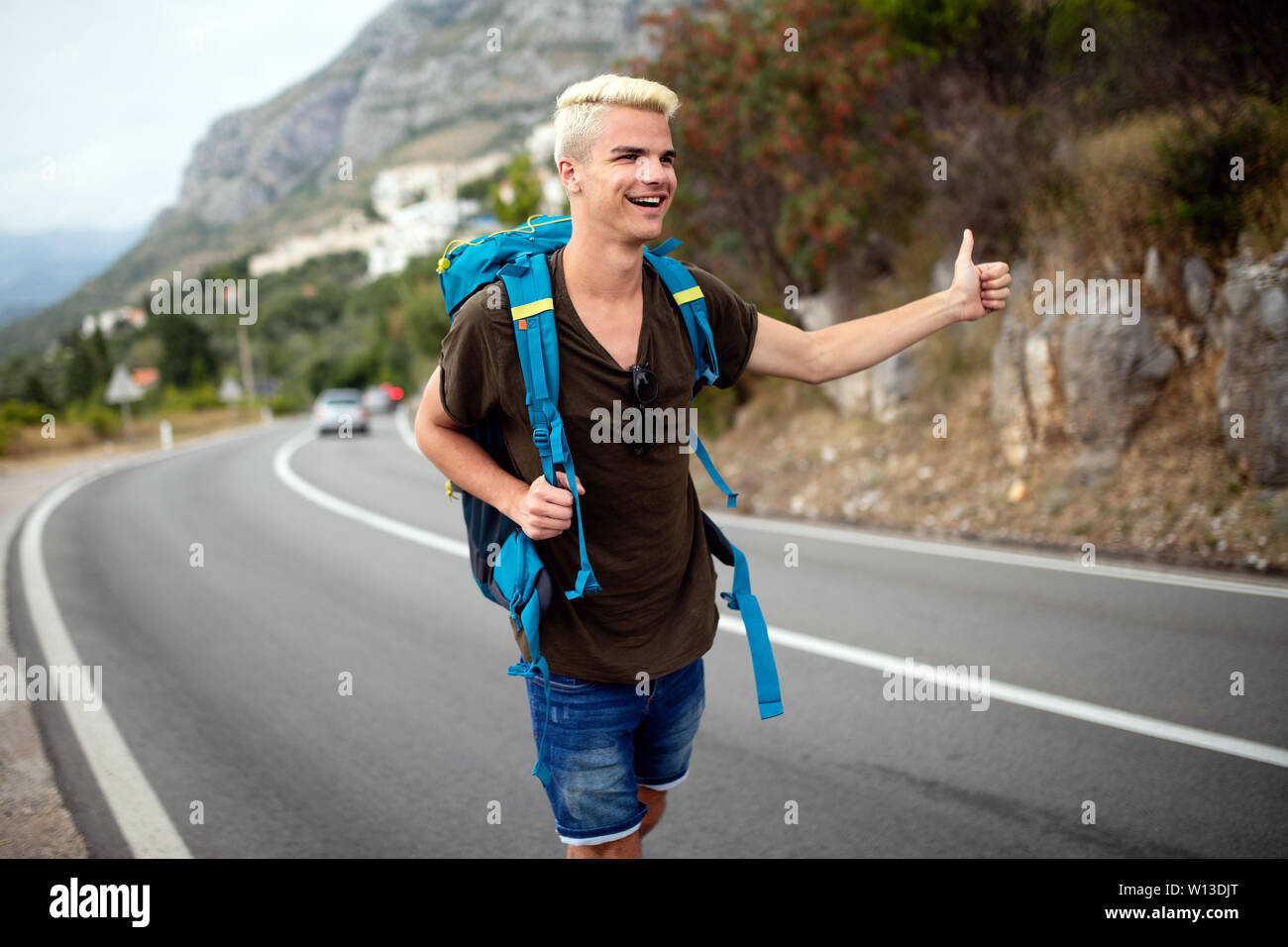Autostop giovane viaggiatore uomo cercare di cattura auto su una strada forestale Foto Stock