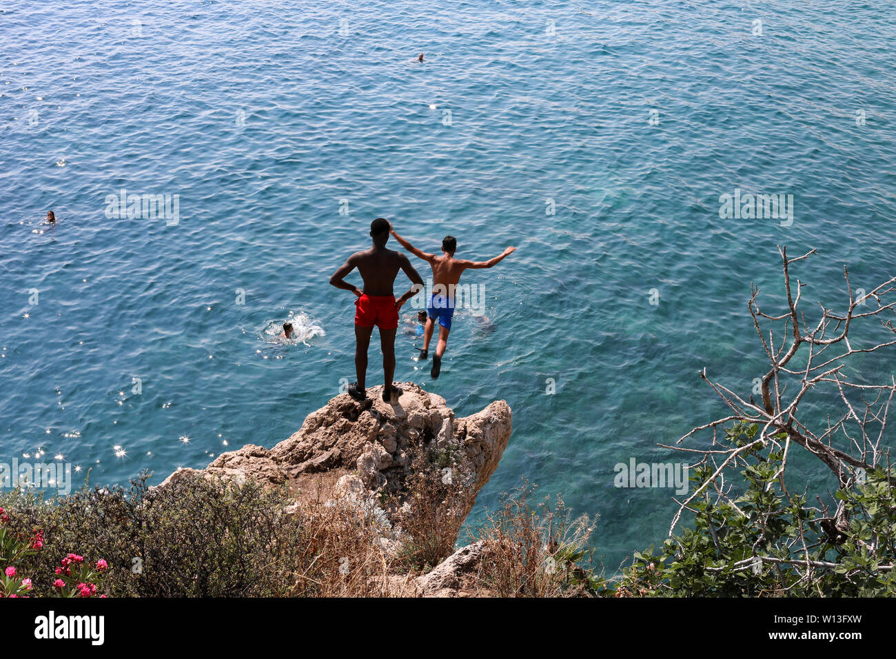 Giovani uomini cliff jumping alla Baie des Anges di Nizza, Francia Foto Stock