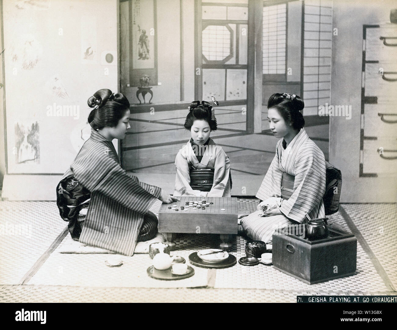 [ 1890 Giappone - il gioco del Go ] - Due giovani donne in kimono e acconciature tradizionali sono la riproduzione di un gioco del go. Un terzo donna guarda a. Una pentola di acqua viene mantenuto caldo sul hakohibachi, un braciere racchiuso in una scatola di legno. Xix secolo albume vintage fotografia. Foto Stock