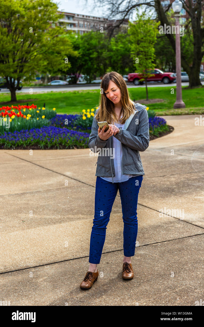 Giovane donna in piedi che guarda verso il basso flowersat il suo telefono in un parco. Foto Stock