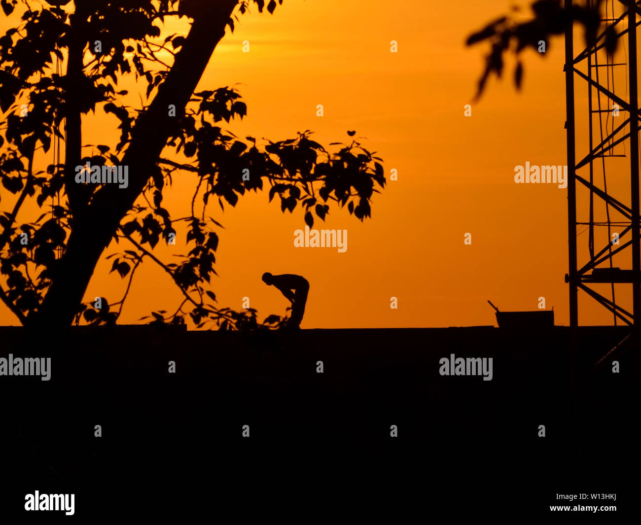 Sagome di una gru e lavoratore edile su un sfondo al tramonto Foto Stock