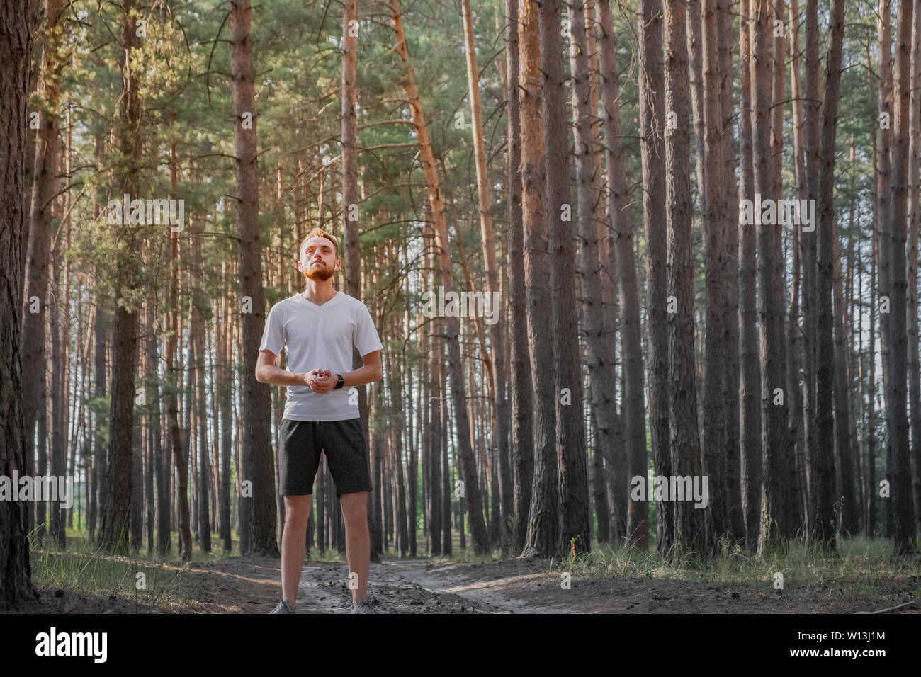 Giovane uomo godendo della natura durante un periodo di riposo a fare jogging nella foresta. Ritratto di una persona di sesso maschile in piedi in una foresta di pini in una giornata di sole Foto Stock
