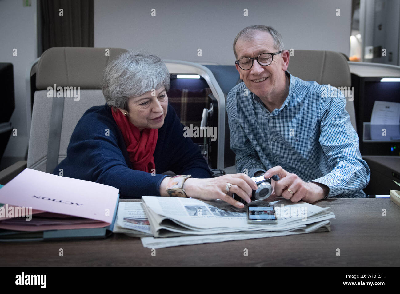 Il primo ministro Theresa Maggio guarda le foto del Vertice G20 presi da suo marito, Filippo come essi volare indietro dalla riunione dei leader mondiali di Osaka in Giappone. Foto Stock