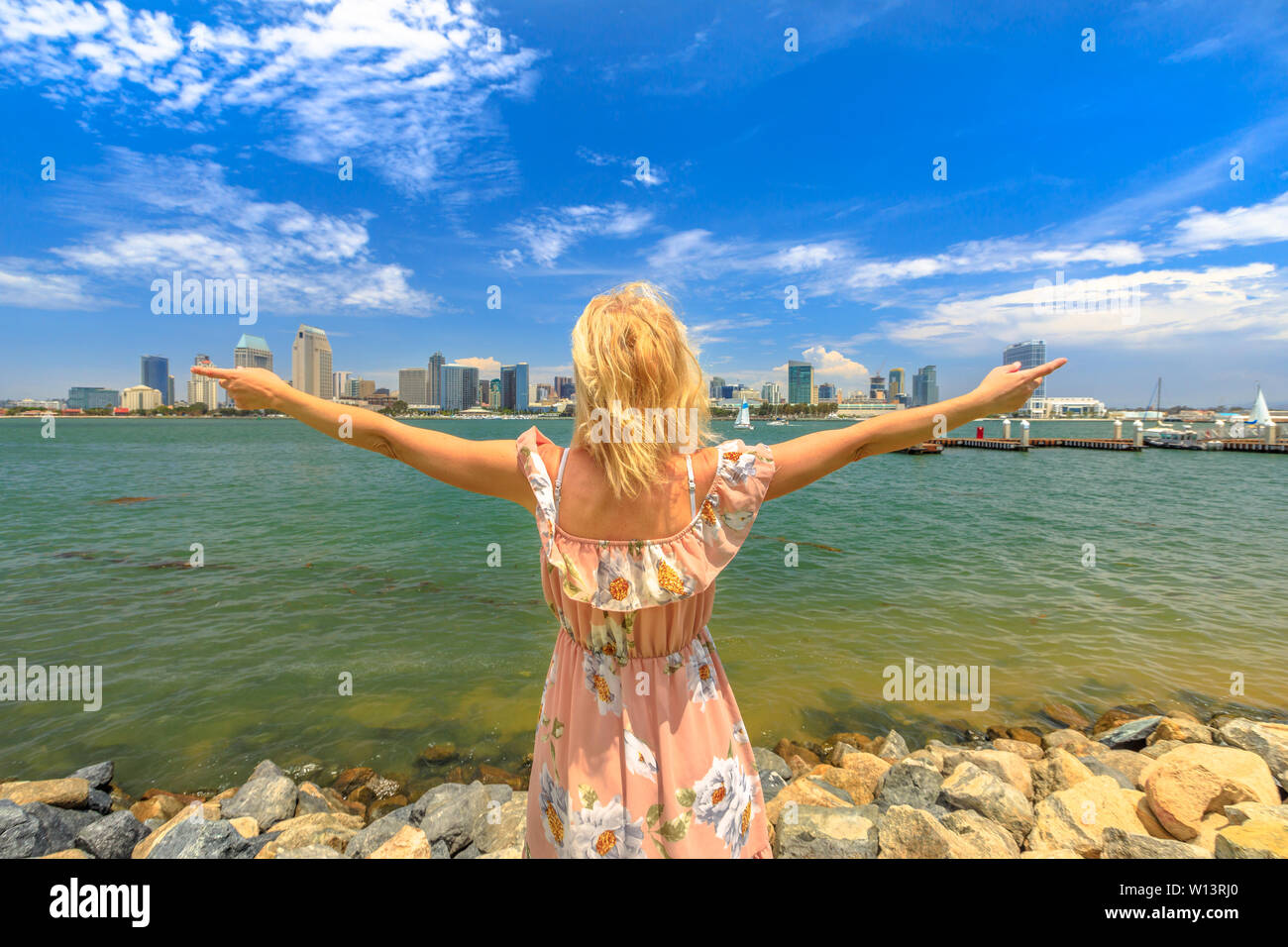 La bionda signora godendo a San Diego skyline del centro con grattacieli in California, Stati Uniti d'America da Coronado Island. Donna turistica in estate le festività americane Foto Stock