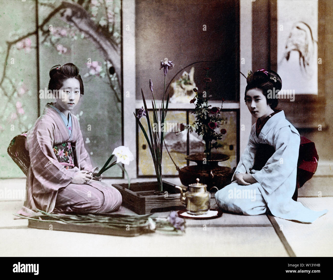 [ 1890 Giappone - dimostrazione di Ikebana ] - Ikebana o giapponese tradizionale omaggio floreale. Due donne in kimono sono disponendo dei fiori mentre è seduto sul tatami (riso tappetini). In retro shoji (carta sliding door) decorato con un dipinto di fiori può essere visto. Xix secolo albume vintage fotografia. Foto Stock