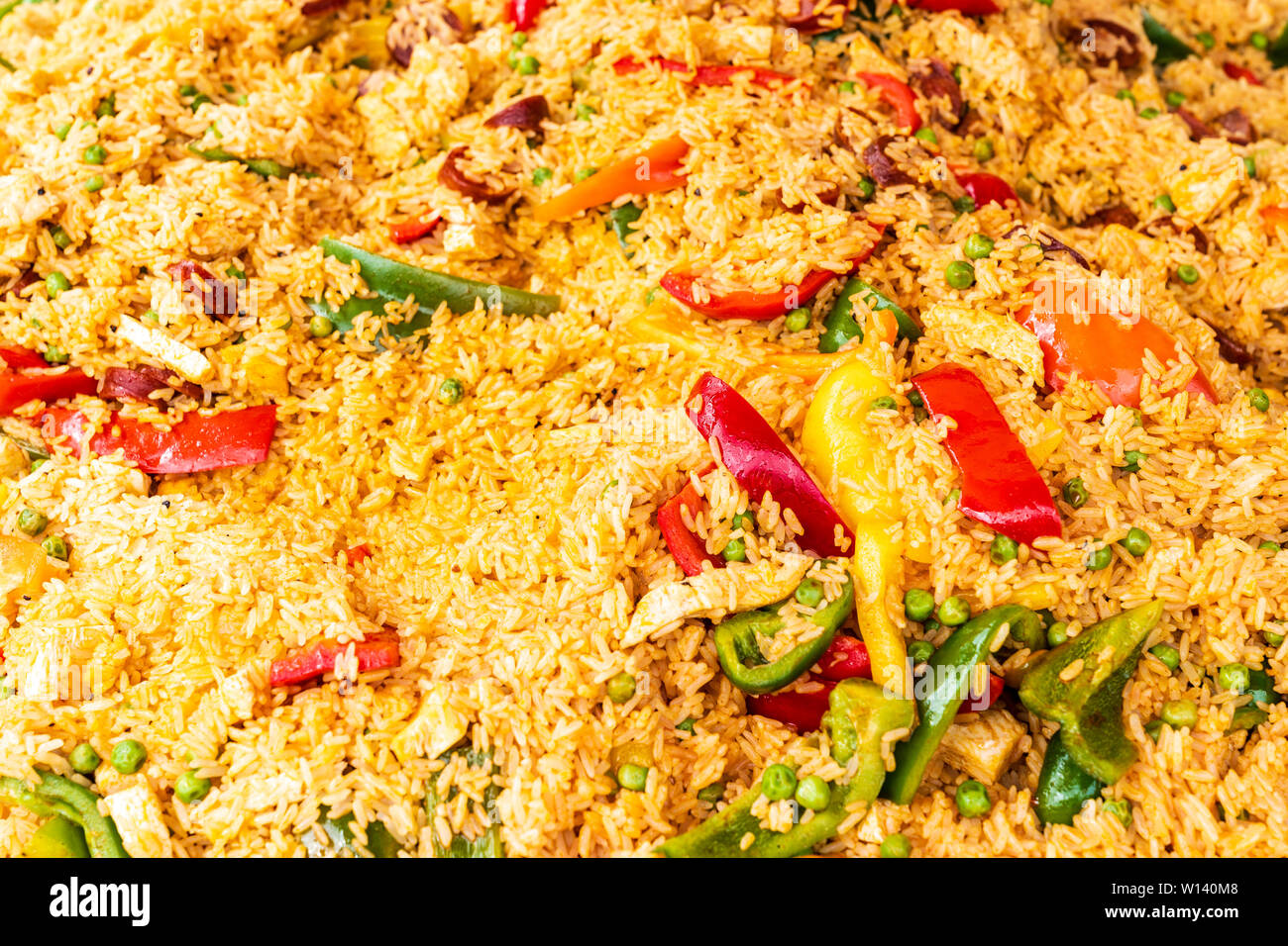 Il cibo vicino, grandi quantità di paella di riempimento del telaio, riso dorato, con il rosso, arancione, giallo e i peperoni verdi con dei piselli. Foto Stock