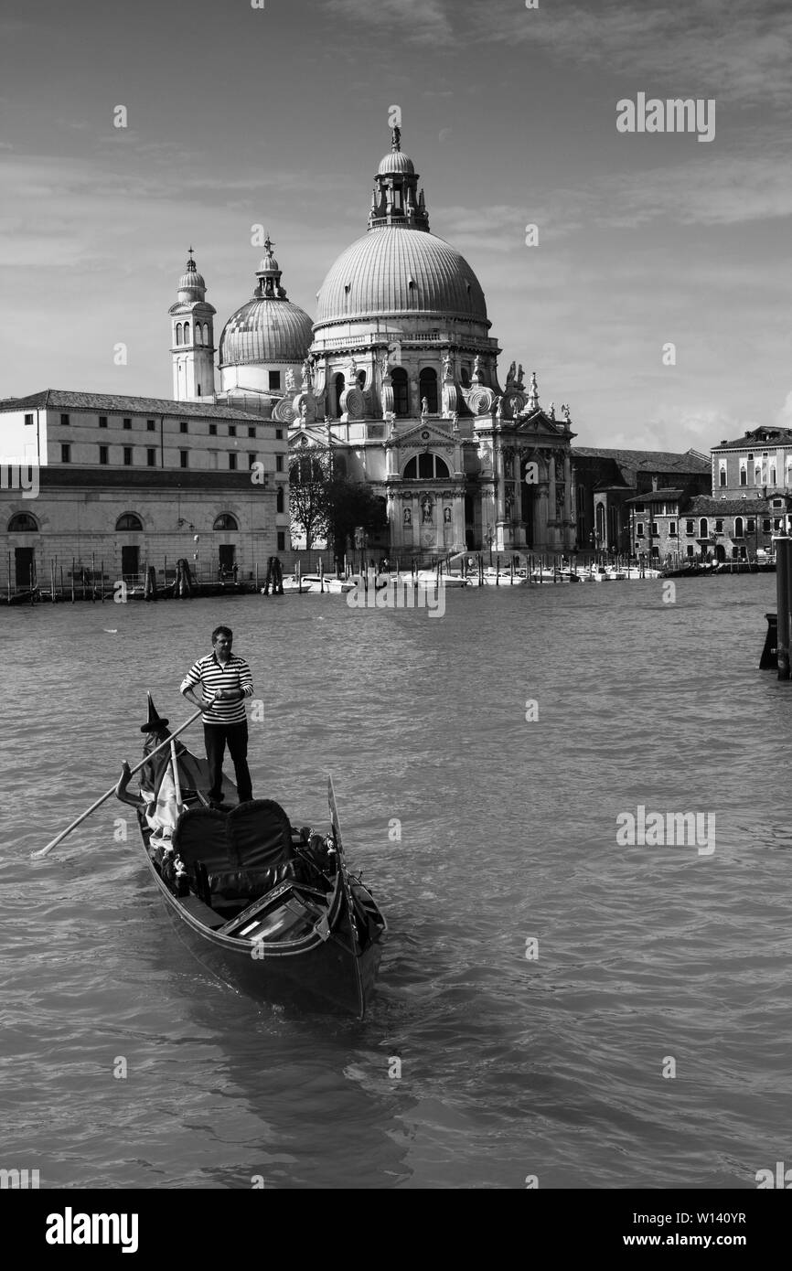 Una gondola e gondoliere sul Canal Grande di Venezia con la chiesa di Santa Maria della Salute in background. Foto Stock