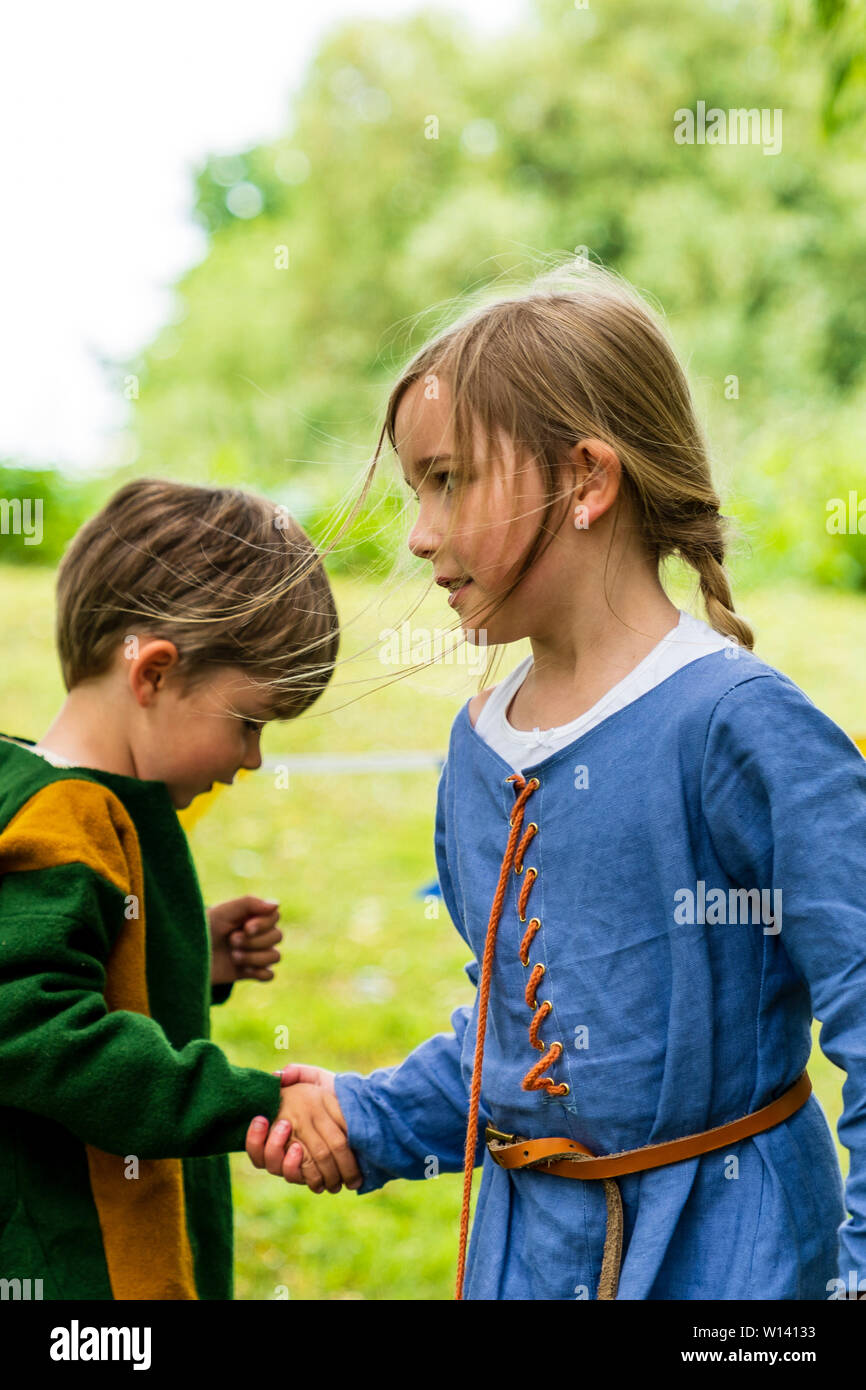 Due bambini, boy, 3-4 anni, e una ragazza, 5-6 anni, vestito in abiti medievali, tenendo le mani che corre intorno a ogni altro. Foto Stock