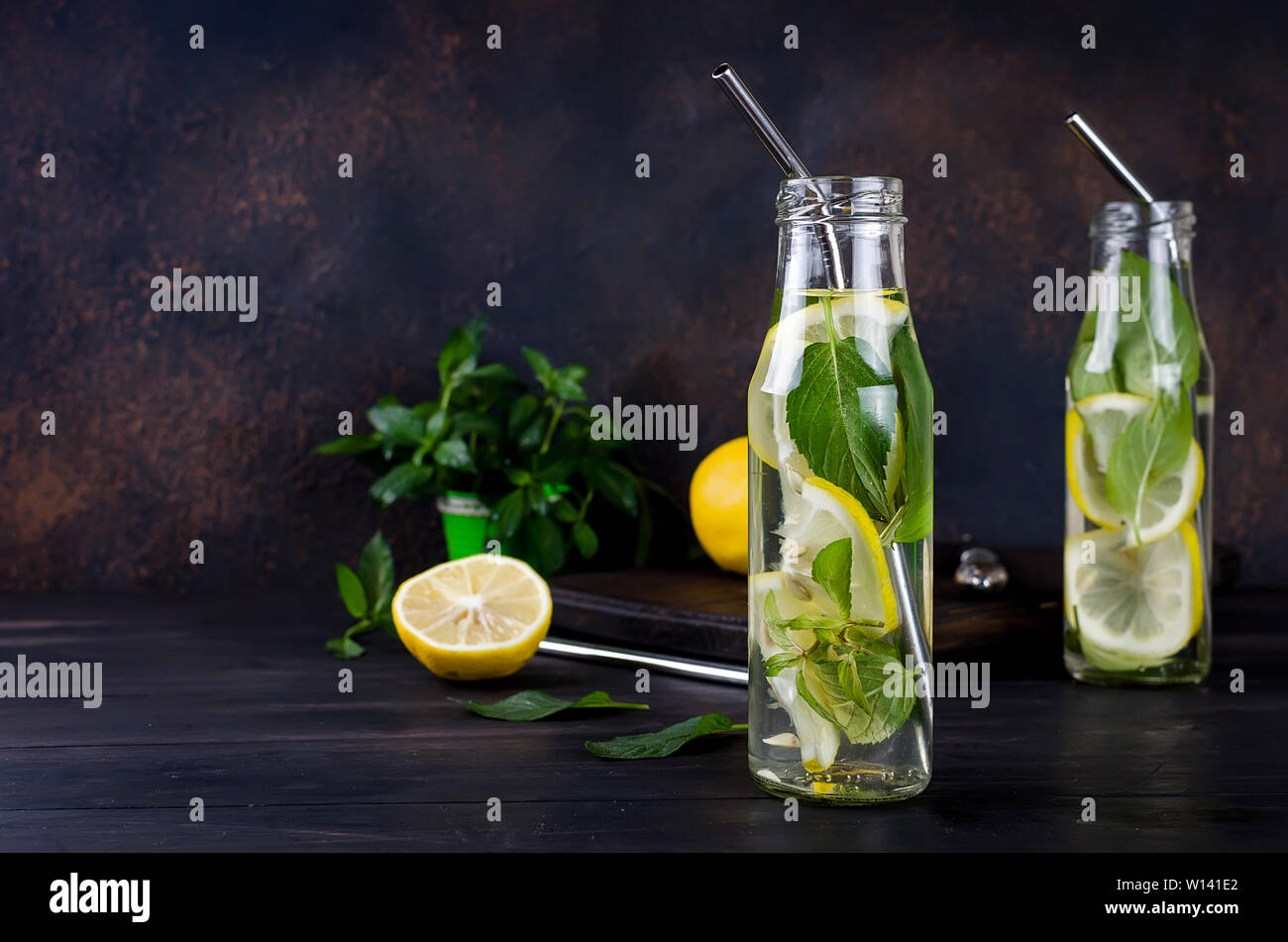 Freschi cocktail mojito bevande in bottiglie e ingredienti, limone e menta in gronda bascet su sfondo scuro, cocktail bibite estive concept Foto Stock