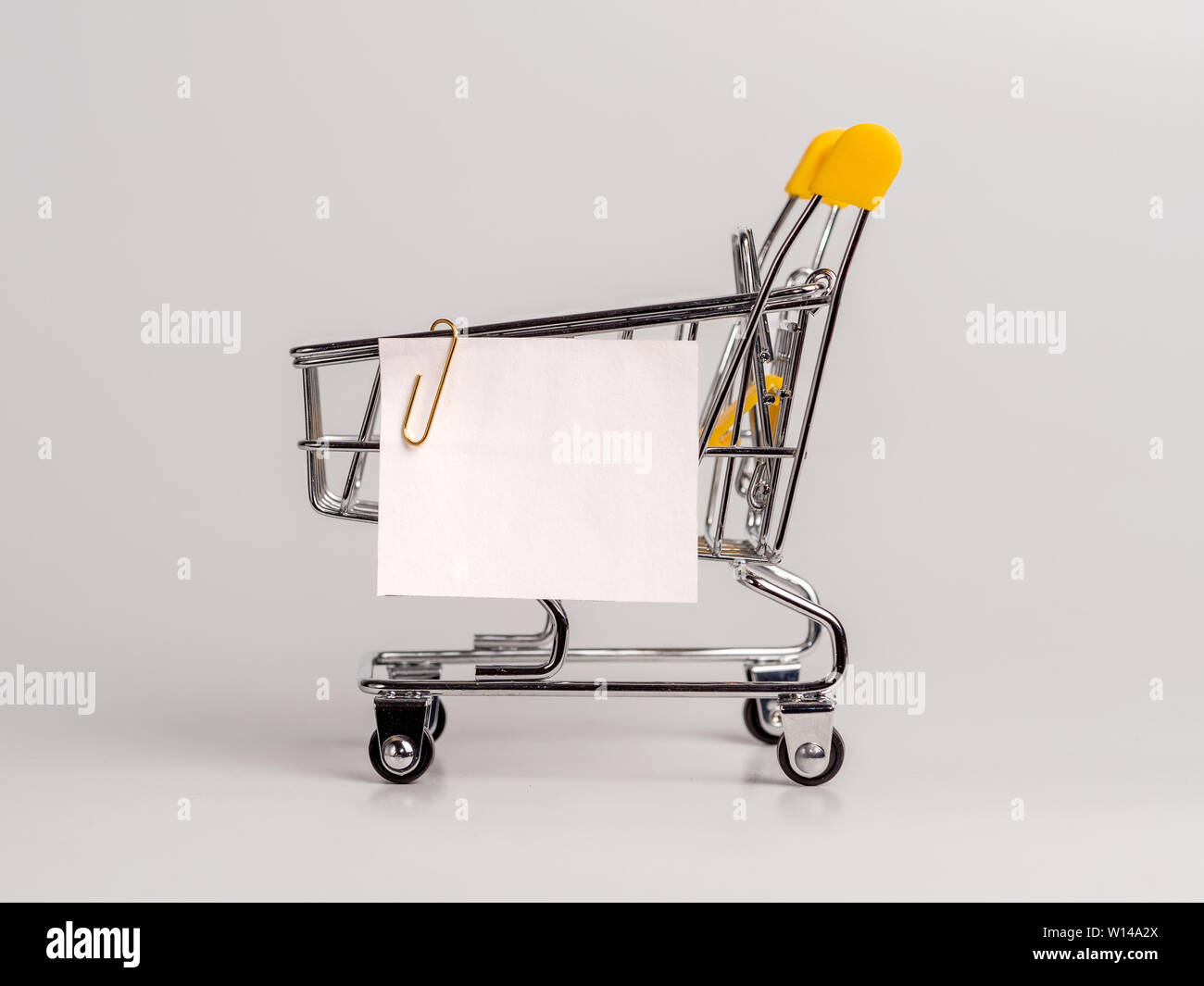 Carrello spesa e white paper nota elenco isolato su sfondo bianco. Il concetto di shopping su luce sfondo monocromo. Vuoto di carta bianca nota su carrello. Copia spazio per il testo o il design. Foto Stock