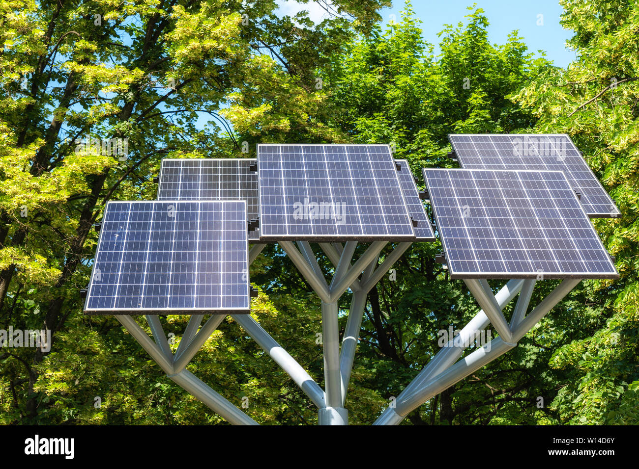 Pannelli solari su un supporto contro il fogliame verde in un parco cittadino, moduli fotovoltaici, sostenibile fonte di energia rinnovabile. Foto Stock