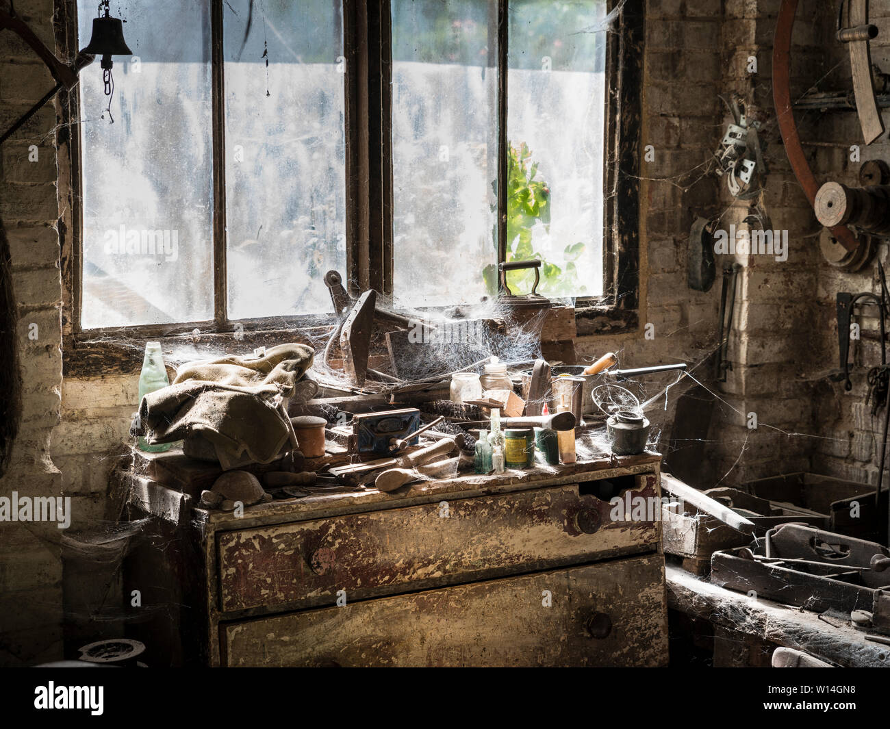 Un workshop abbandonati con strumenti polveroso e ragnatele di fronte a una finestra sporca. Foto Stock