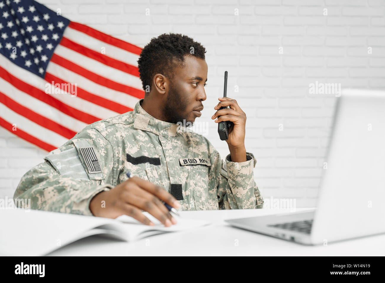Lavoratore di esercito americano la scrittura di documenti utilizzando laptop e Destinazione telecomando radio, parlando con i colleghi. Giovani ranker seriamente guardando e subroutine Foto Stock
