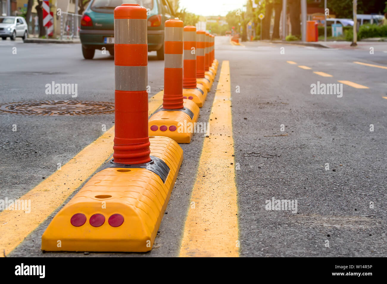 Colonne con uno strato riflettente e giallo marcatura su strada separa il percorso ciclabile dalla parte di automobile della strada. La sicurezza di uno stile di vita attivo. Foto Stock