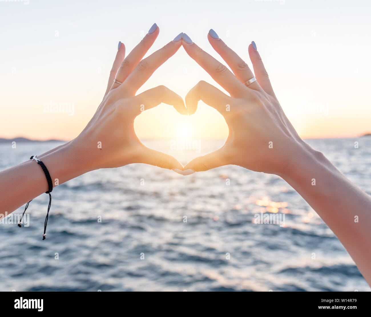 Giovani donne belle mani sullo sfondo del mare visualizza il simbolo del cuore. Vacanza - concetto. Foto Stock