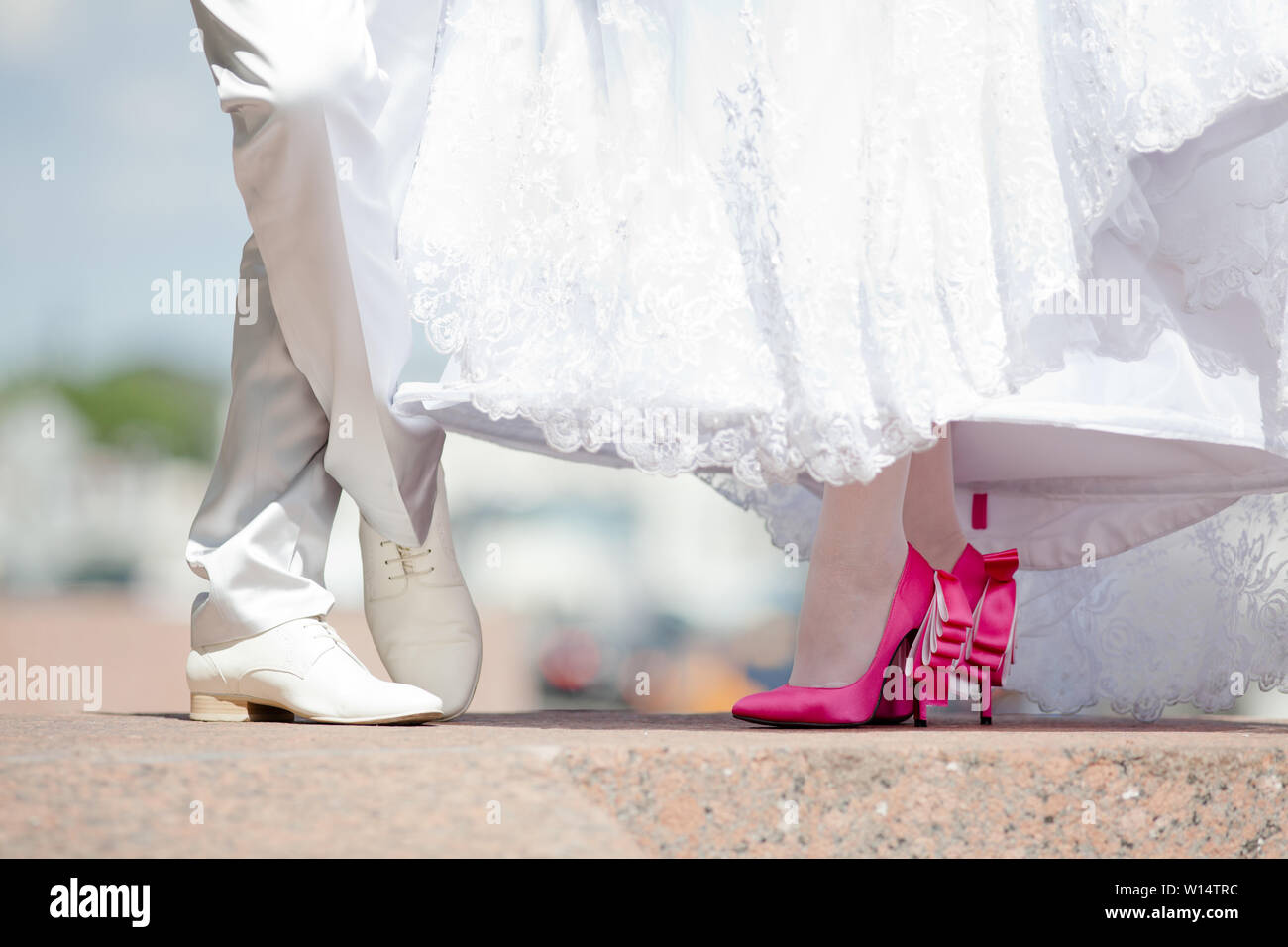 Gambe di lo sposo in bianco scarpe e pantaloni e spose in crimson tacchi con un bianco di neve, coulisse di un abito da sposa. Colpo all'aperto Foto Stock