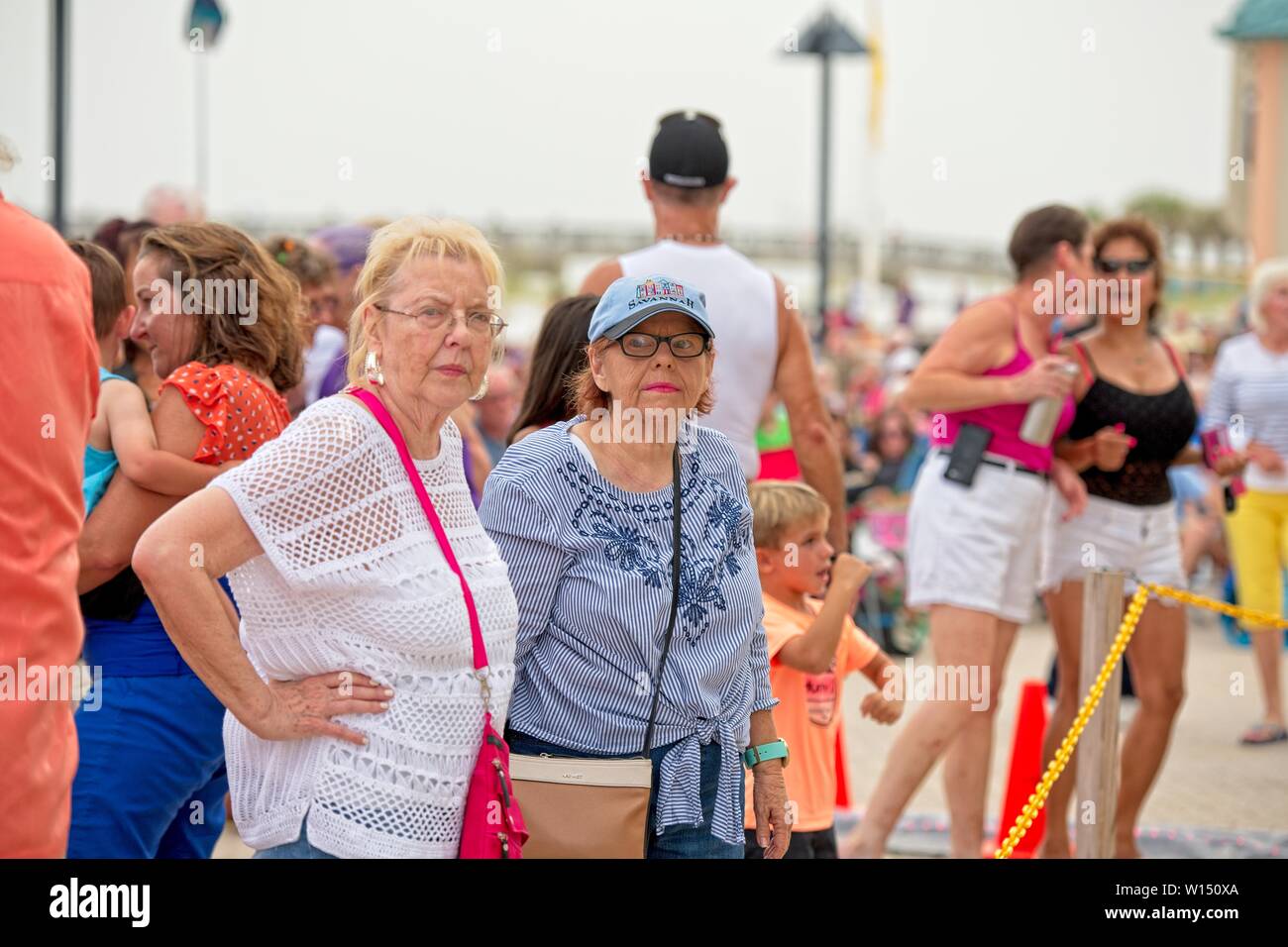 Due donne anziane in una folla di persone alla spiaggia che guardano avanti con intenso sguardo sul loro volto Foto Stock