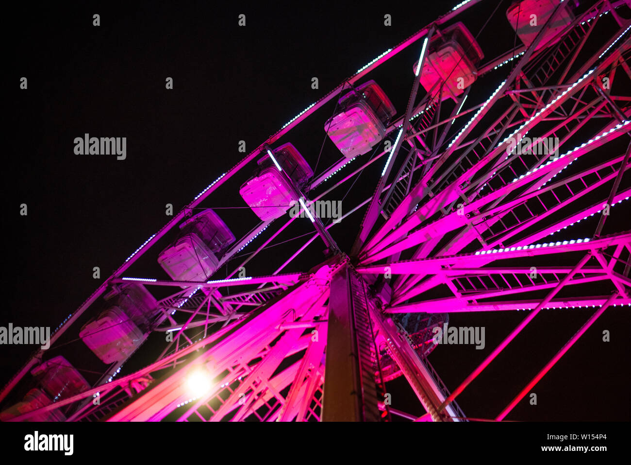 Primo piano di una rosa luminoso ruota panoramica Ferris illuminato contro un cielo scuro durante un festival in una città Foto Stock