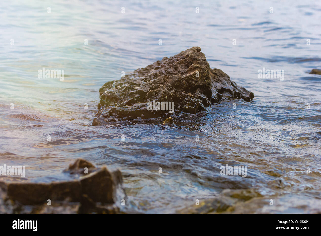 La pietra vicino al fiume. Onde eseguire sul litorale. Tramonto d'estate. I raggi del sole si riflettono nell'acqua Foto Stock