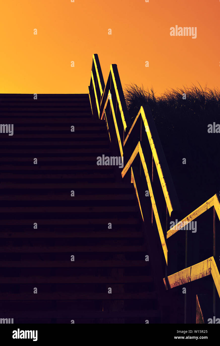 Spiaggia di scale in legno a golden ora in condizioni di luce scarsa. Salendo le scale oltre le dune con erba alta Foto Stock