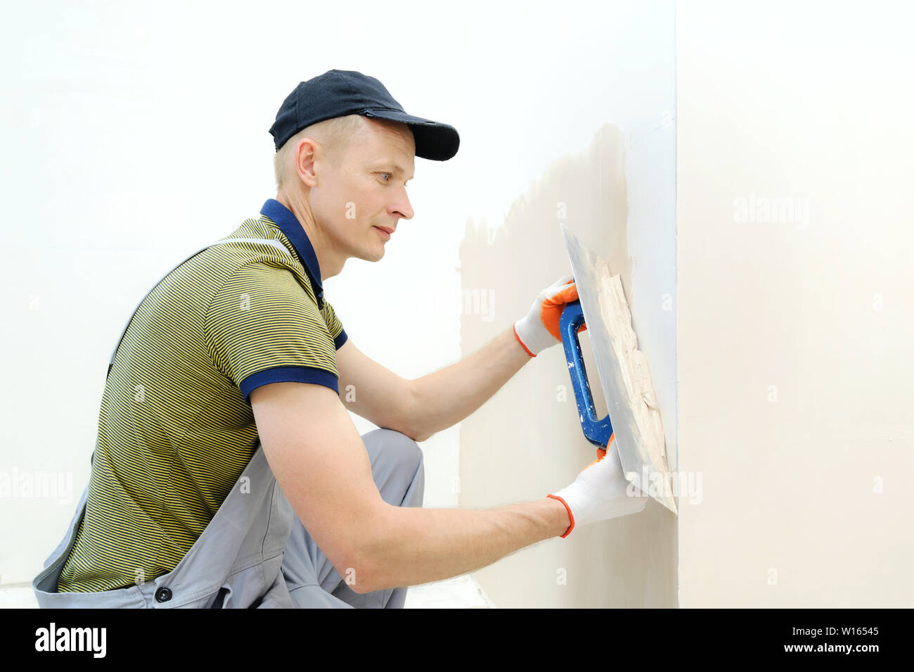 Un lavoratore è intonacatura di una parete in un appartamento con una cazzuola a lungo. Foto Stock