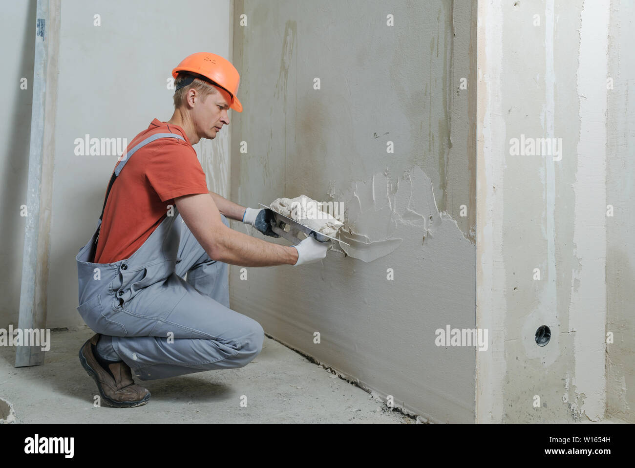 Lavoratore è mettere un gesso su una parete. Egli è con una cazzuola a lungo. Foto Stock