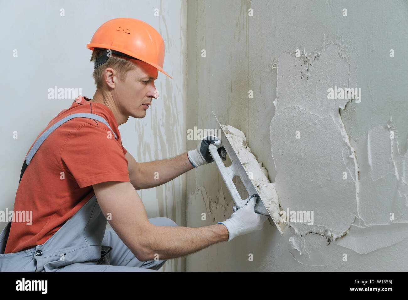 Lavoratore è mettere un gesso su una parete. Egli è con una cazzuola a lungo. Foto Stock