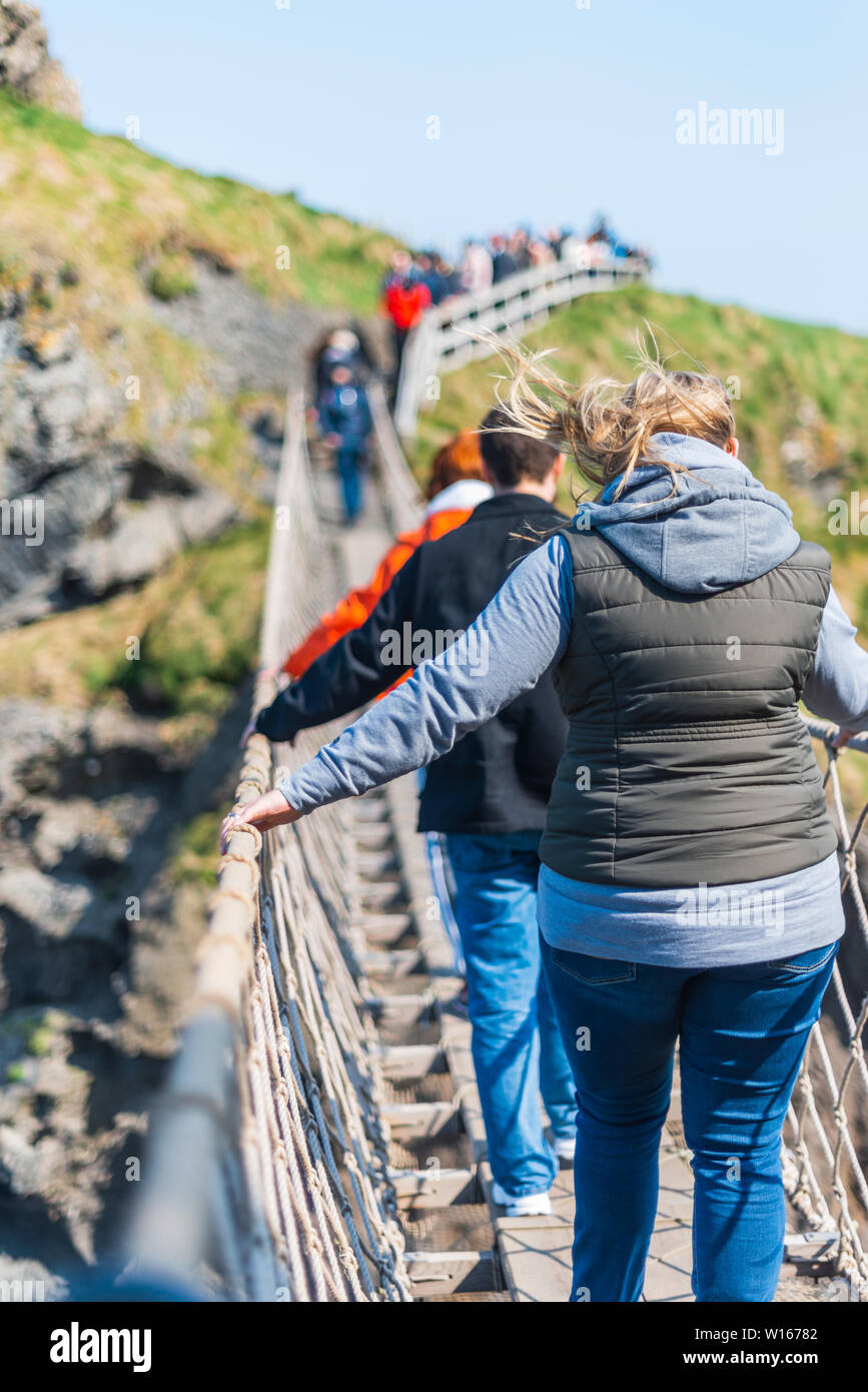 Irlanda del Nord, Regno Unito - 8° aprile 2019: spaventato i turisti attraversare il pericoloso ma bella Carrick-a-Rede ponte di corde Foto Stock