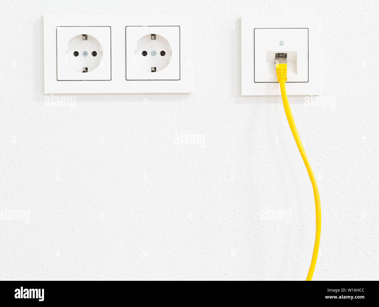 Cavo di rete di colore giallo nella presa a muro per ufficio o casa privata  la connessione LAN Ethernet con prese di corrente vista piana su intonaco  bianco sullo sfondo della parete
