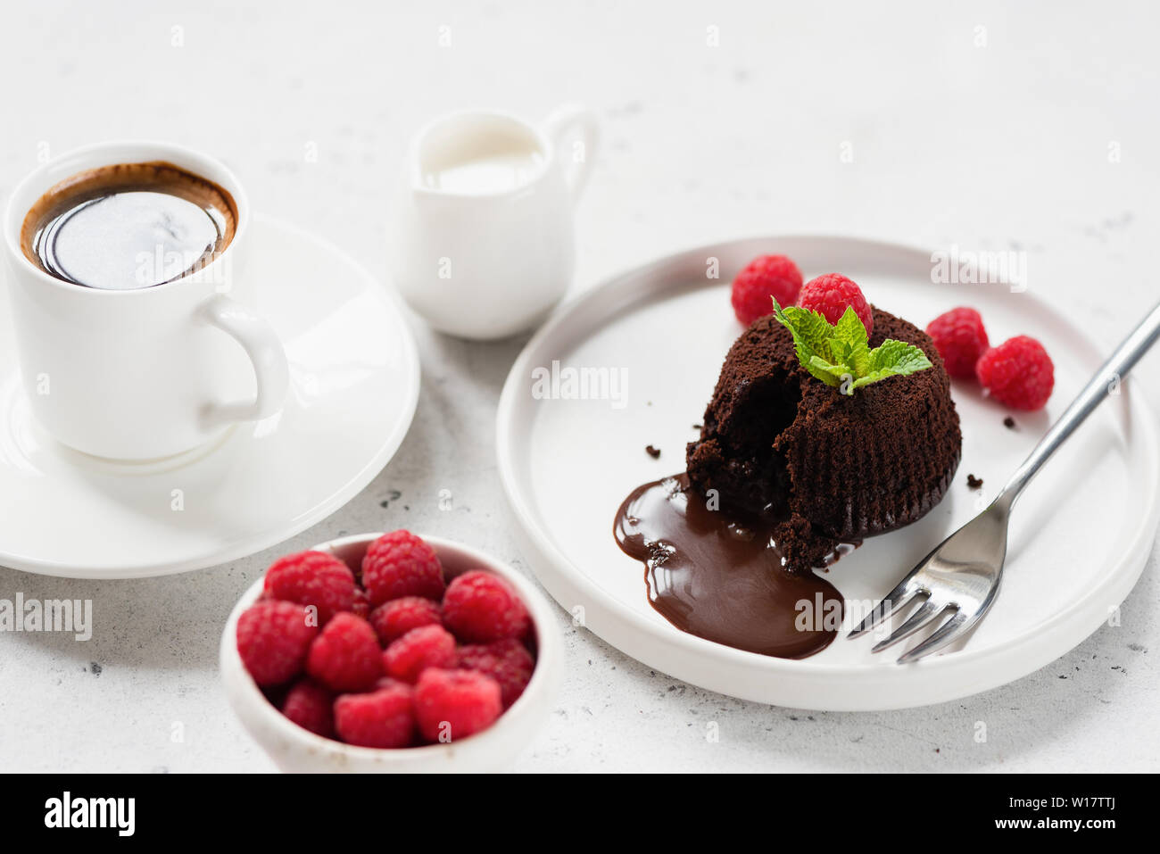 Gustosi dessert al cioccolato fondente o torta di lava sulla piastra bianca servita con tazza di caffè nero, crema di lamponi Foto Stock