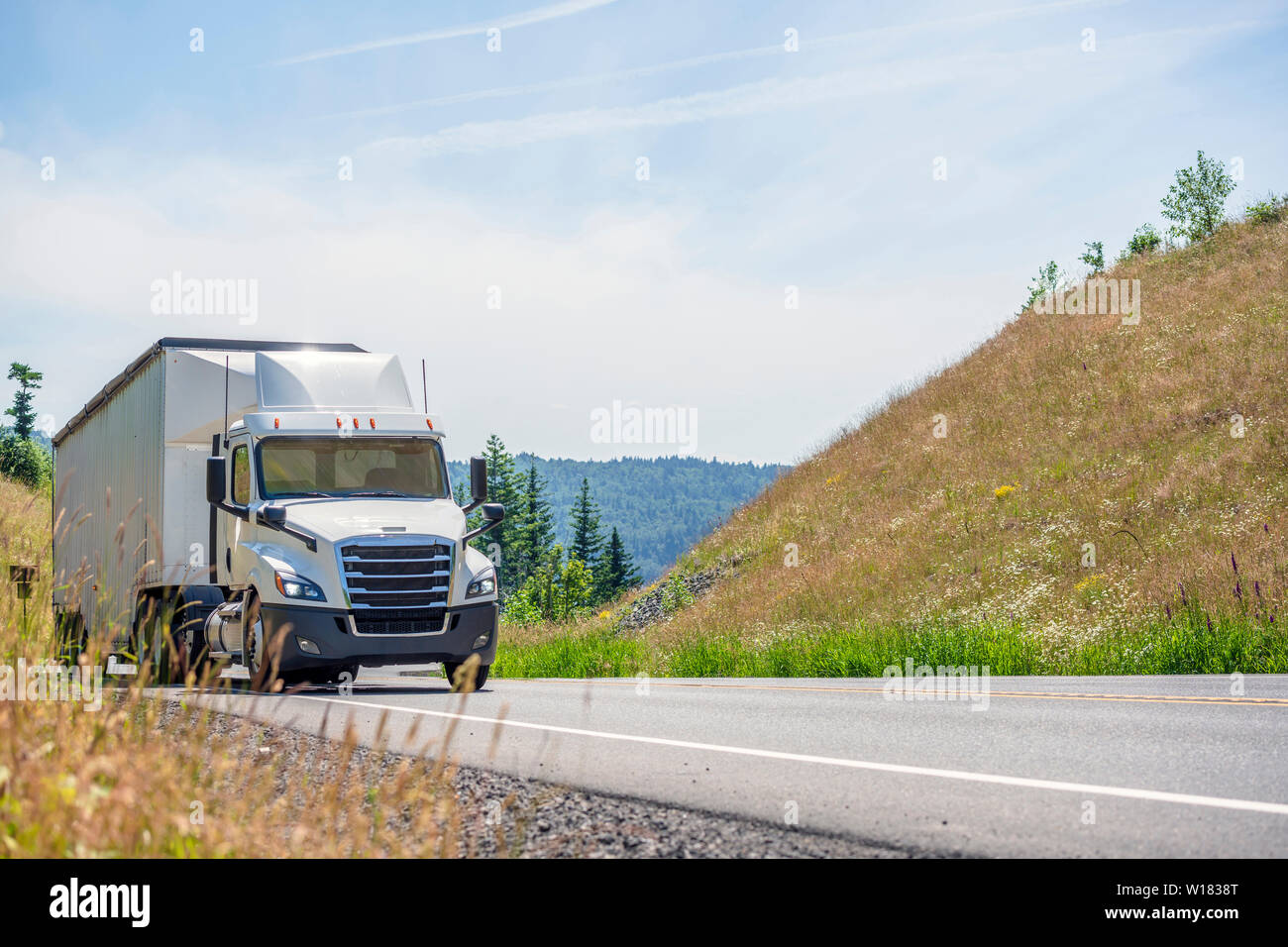 Big Rig bianco cabina giorno semi carrello con spoiler del tetto trasportano enormi coperte rinfusa semi rimorchio si muove in salita sul girando strada tortuosa con giallo g Foto Stock